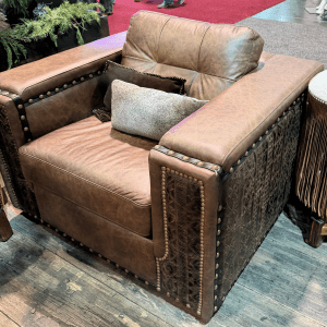 Brown leather armchair with studded nailhead trim and carved side panels, two decorative pillows on the seat.