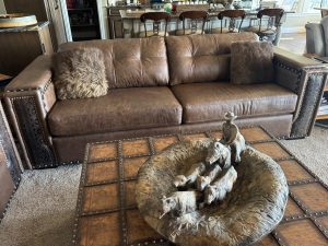 Brown leather tufted sofa with two fluffy gray pillows in a living room; decorative rock sculpture on a studded wooden coffee table in front of it.