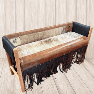 Vintage brown leather sofa with black fringe and wood frame against light wood panel backdrop, on a wooden floor/wall.