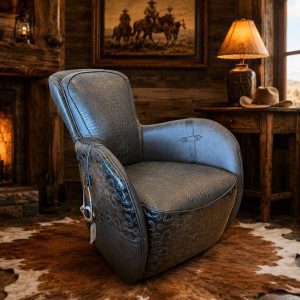 A dark leather recliner with a textured crocodile pattern sits in a rustic cabin room, with a wooden desk, hat, and lamp in the background.